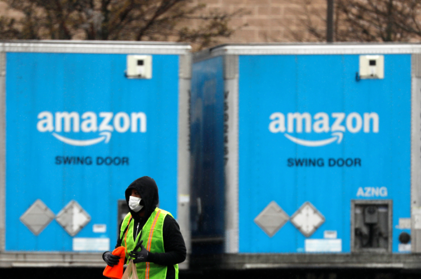 A worker in a face mask walks by trucks parked at an Amazon facility as the global coronavirus outbreak continued in Bethpage on Long Island in New York