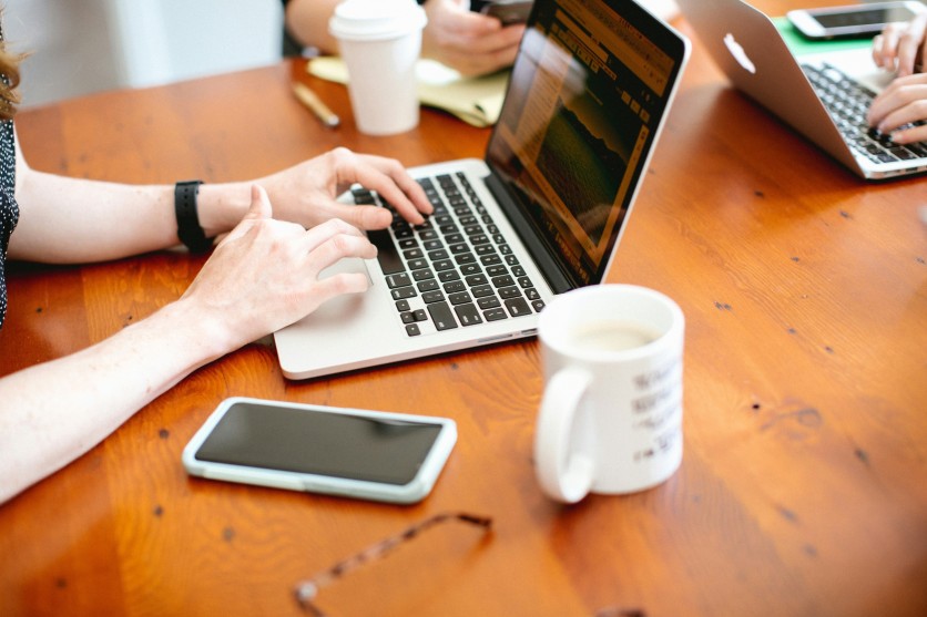 Close-up of people working on laptops at a wooden table