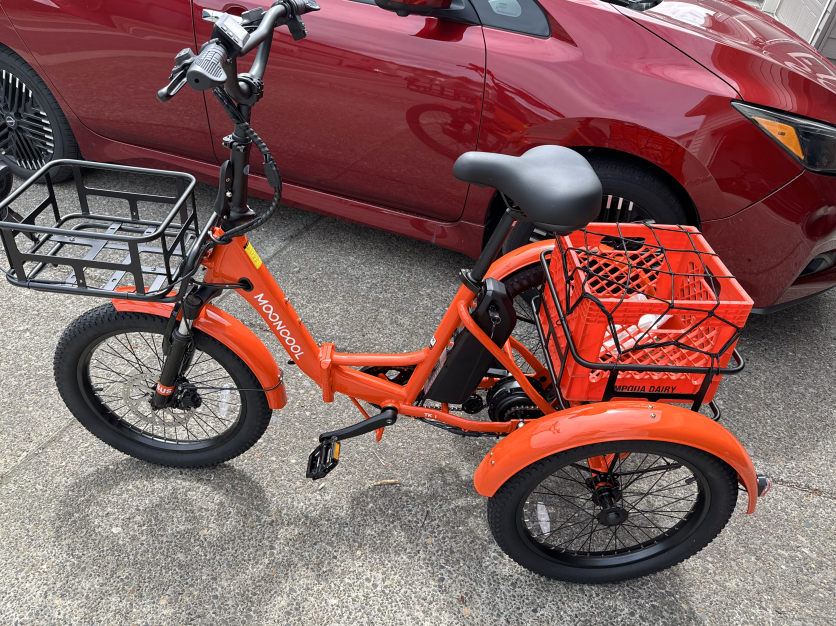 Orange folding electric trike in front of a red car