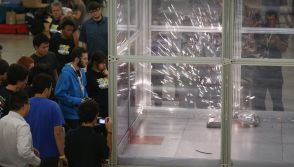 People watch as sparks fly from robots when they crash
